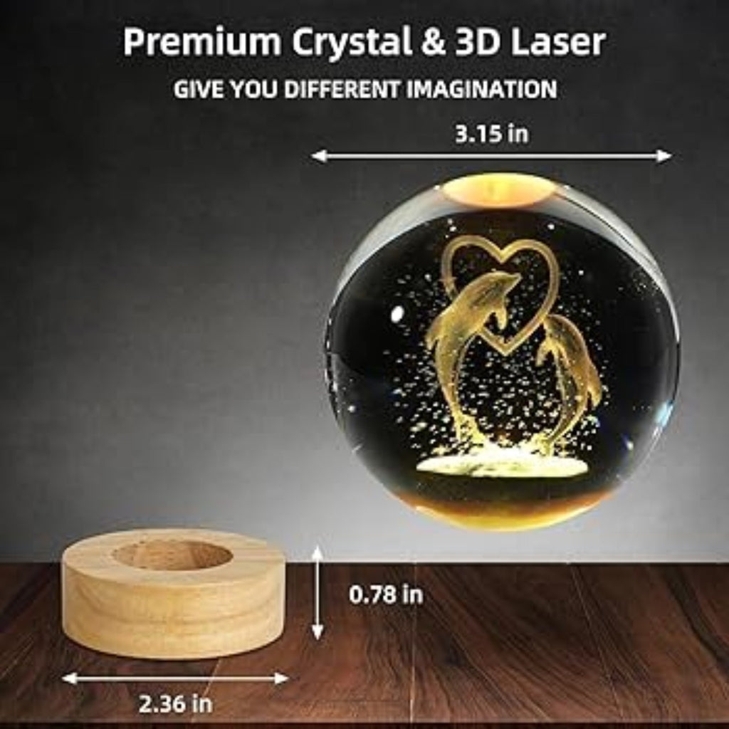 Crystal ball with 3D laser engraving of penguins in a heart shape, placed on a wooden stand with measurements indicated.