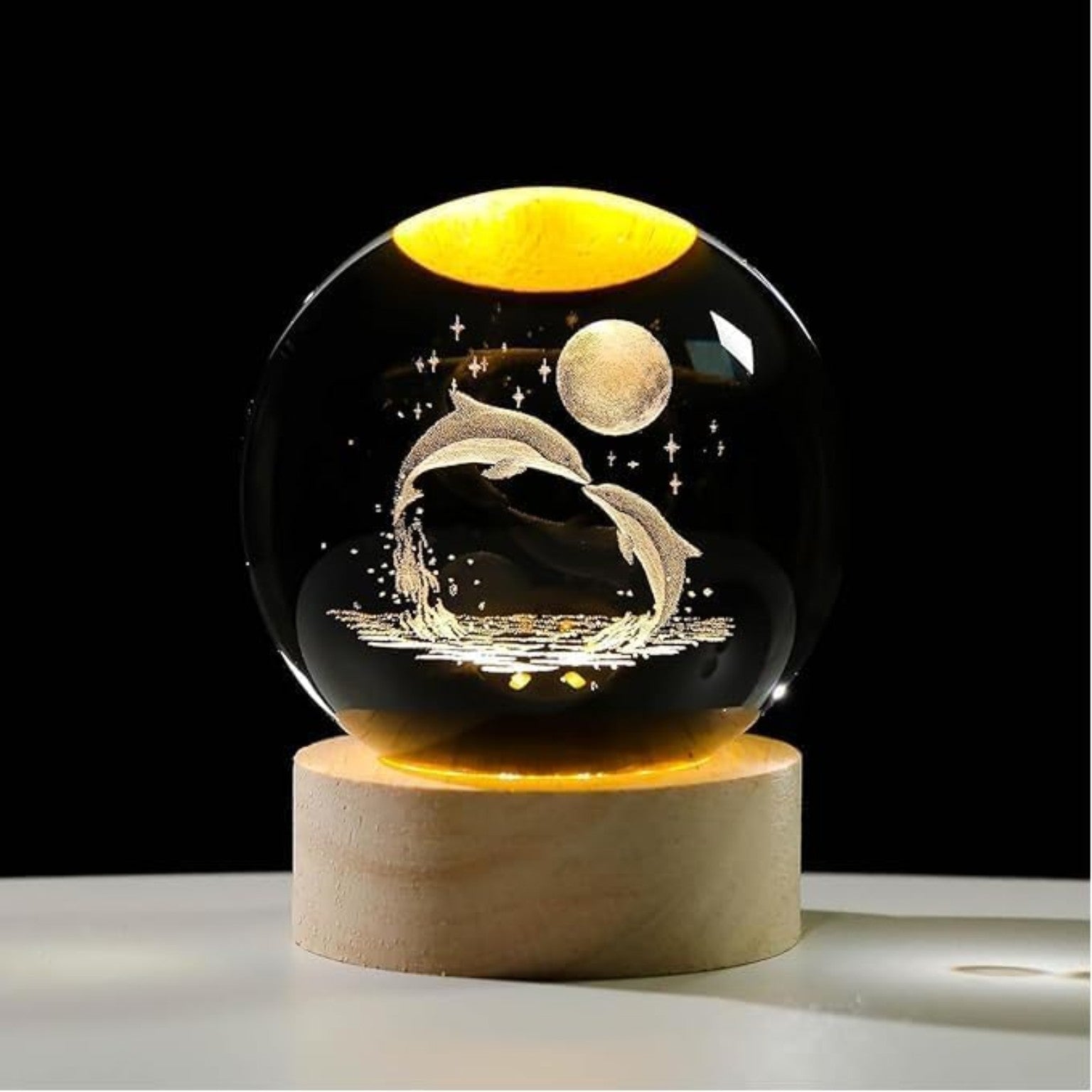 Decorative glass ball with dolphins and moon design on a wooden base against a dark background