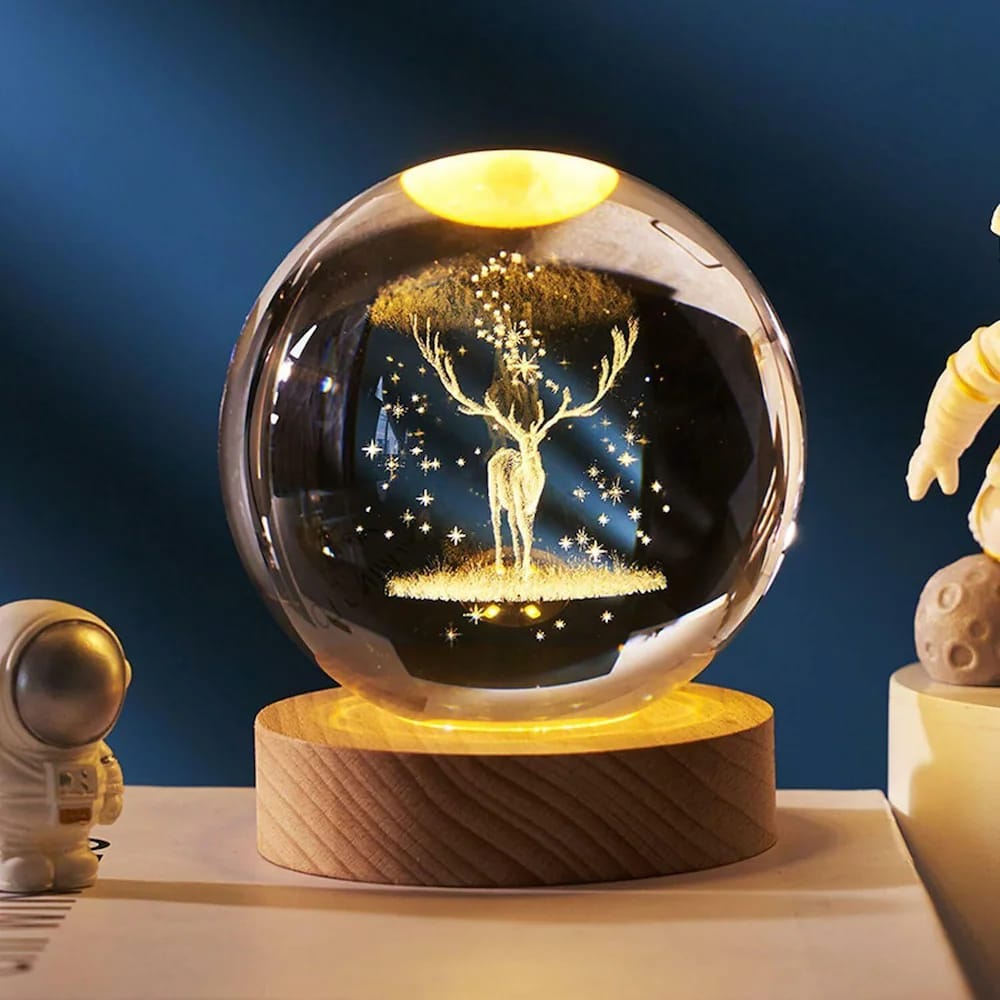 Decorative glass ball with a deer silhouette on a wooden base against a dark blue background