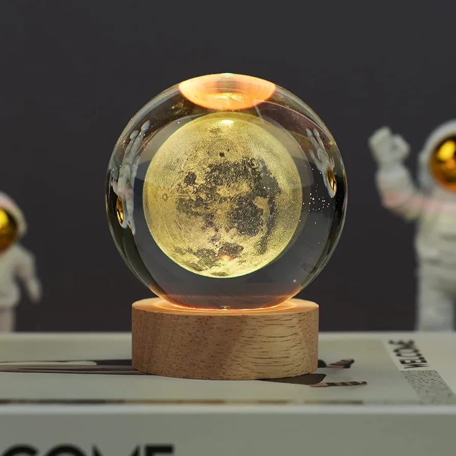 Glass sphere with moon texture on a wooden base, with astronaut figures in the background.