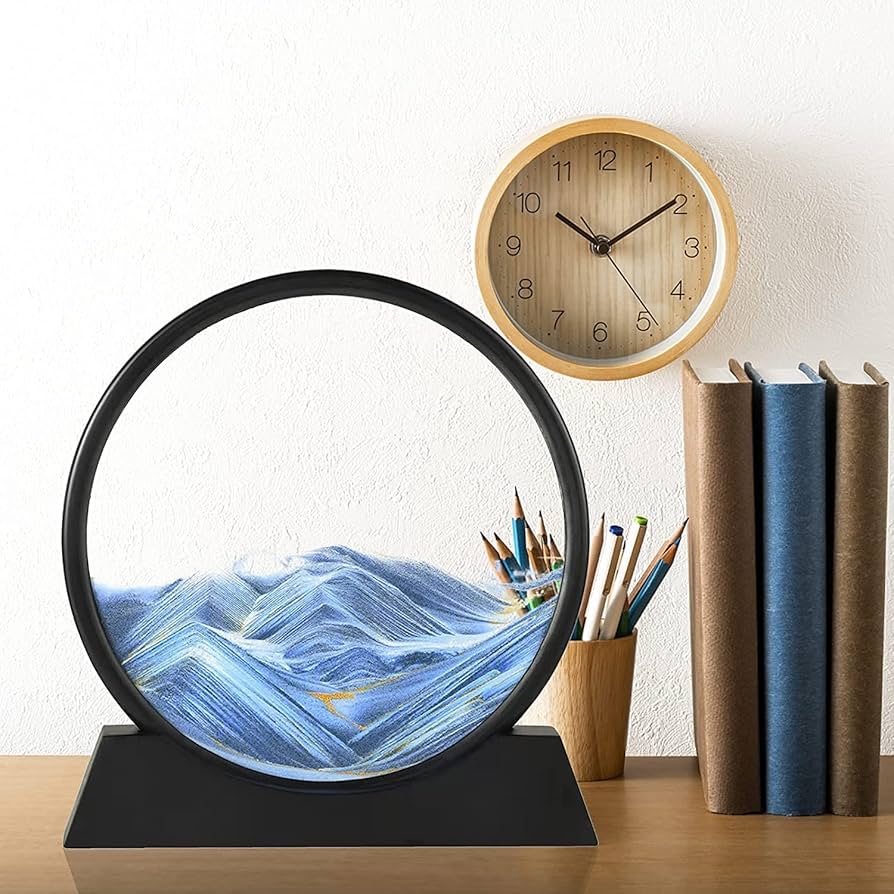 Decorative lamp with mountain design, wooden clock, and books on a table.