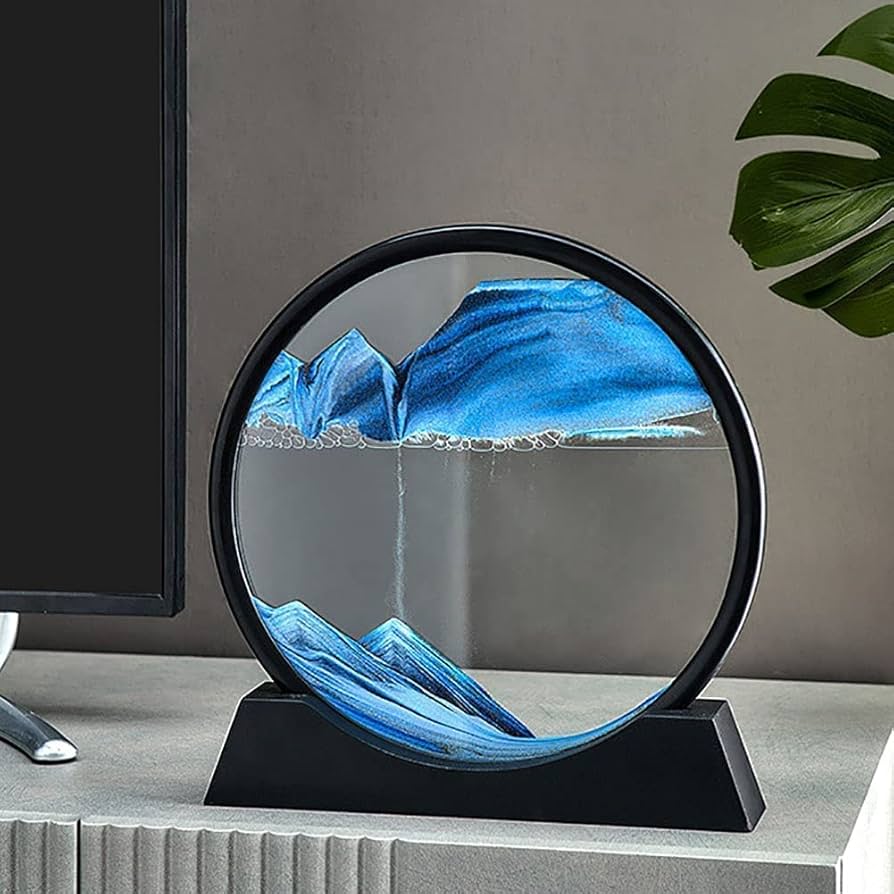 Blue glass sculpture in a circular frame on a gray surface with a plant in the background