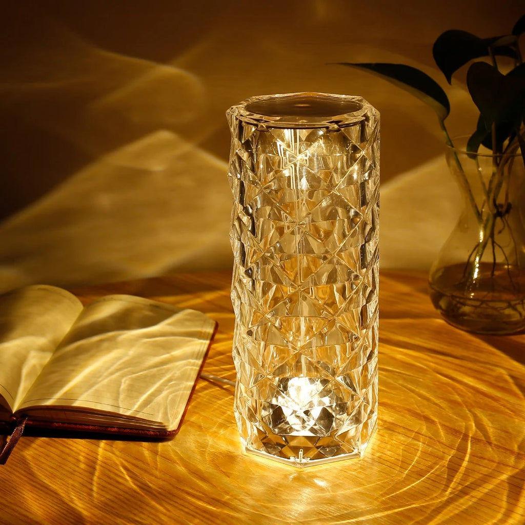 Decorative glass vase with a warm glow on a wooden surface, next to an open book and a plant.